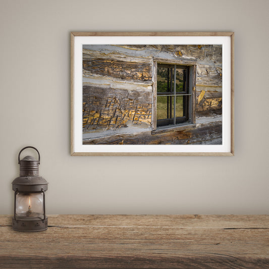 Photography print featuring a vintage window on a weathered log cabin wall, imbued with the peaceful, golden glow of sunset.